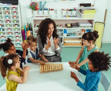 A teacher clapping along as children play a xylophone at a table