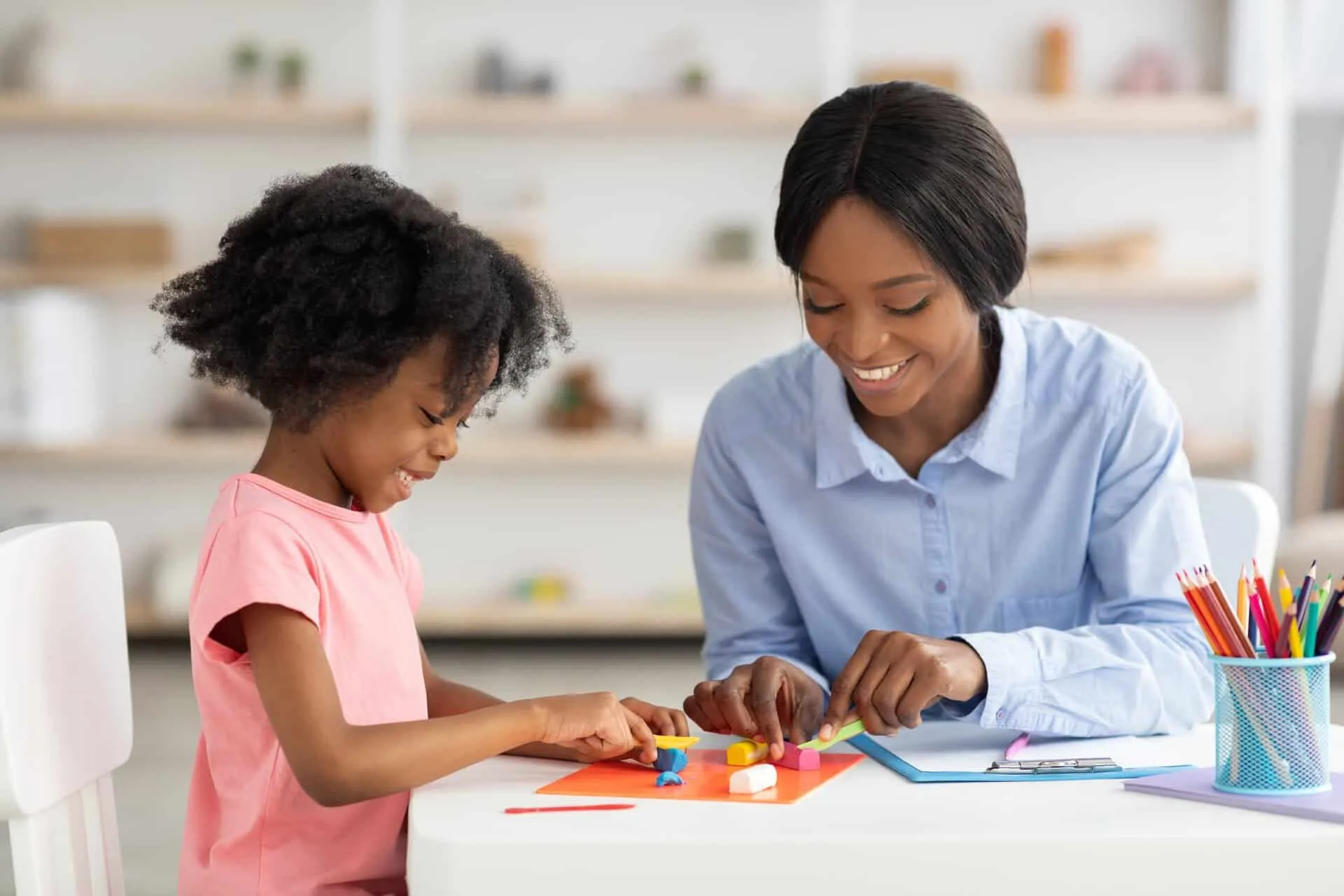 A girl and a teacher playing with play dough at a table