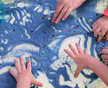 Small hands drawing patterns in blue sand