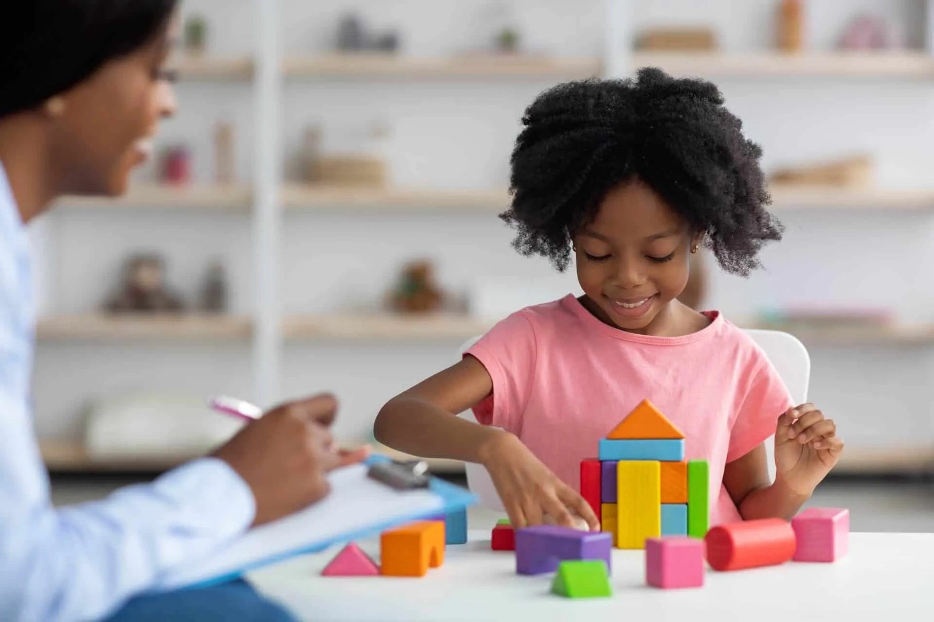 A girl building with colorful blocks while a counselor takes notes