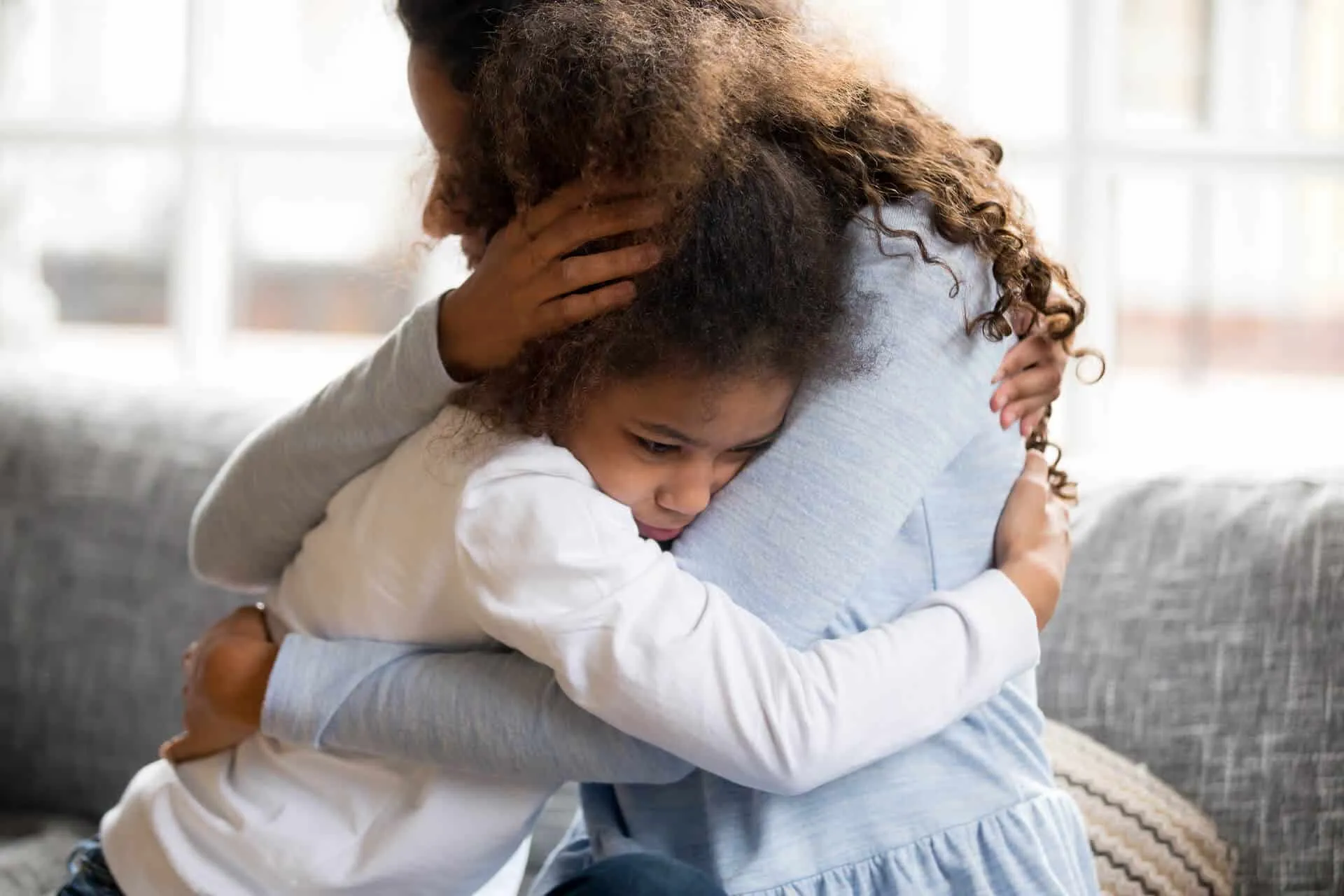 A parent hugging a young girl on a couch