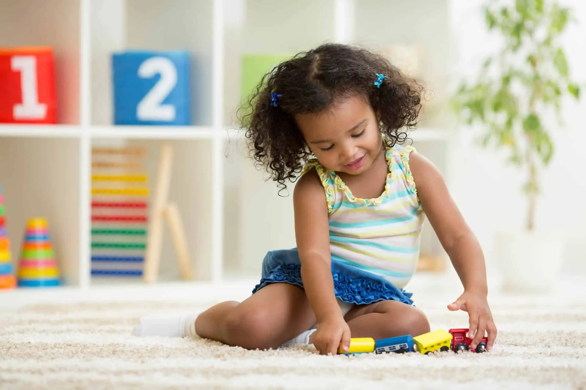A young girl playing with a toy train on a rug
